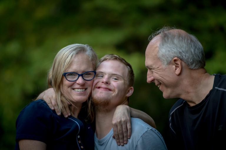 A woman hugging her son and a man smiling at them.